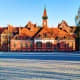 Historic red brick building with clock tower and spired rooftop in European town square under clear blue sky